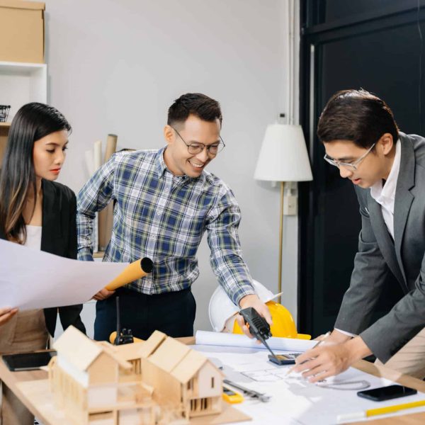 Engineer teams meeting working together wear worker helmets hardhat with on architectural project site and making model house. Asian industry professional team in modern office