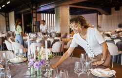 event decorator arranging festive table setting near team working in banquet hall, creative work