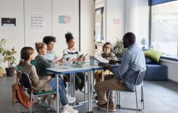 Full length shot of diverse group of children sitting at table with male teacher in modern school classroom