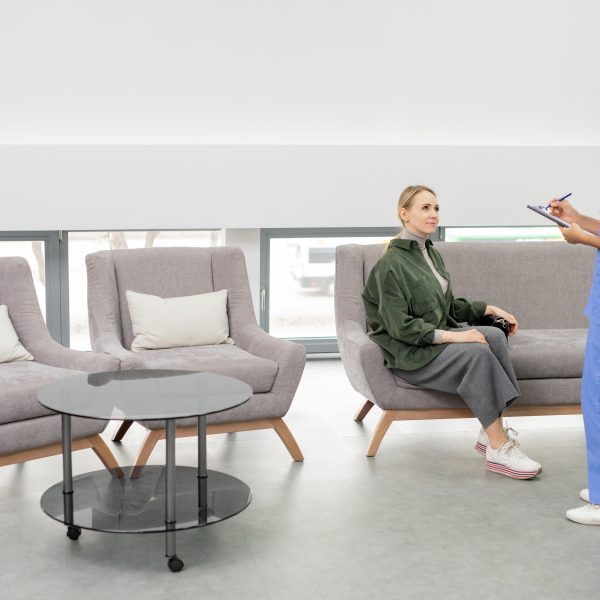 Pretty young brunette assistant in blue uniform writing down name of one of patients in document before medical consultation in clinics