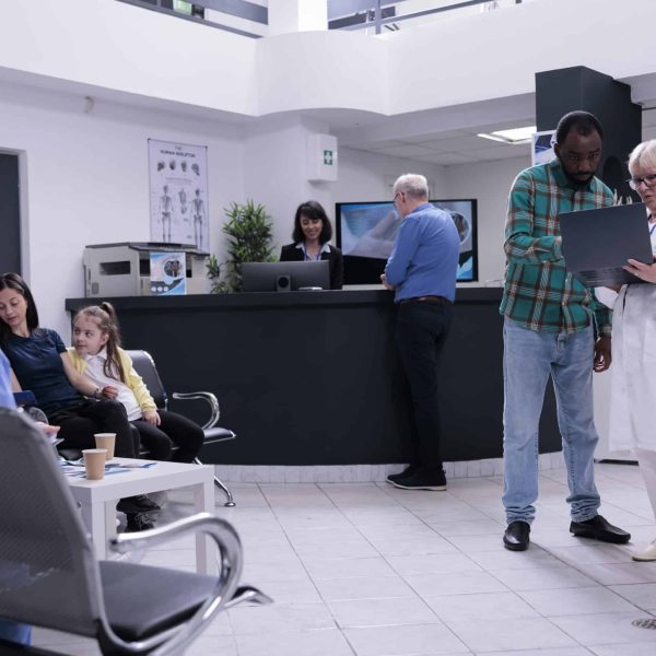 Senior medical doctor holding laptop presenting lab results to african american patient in private practice clinic. Older medic talking with man checking appointment on portable computer.