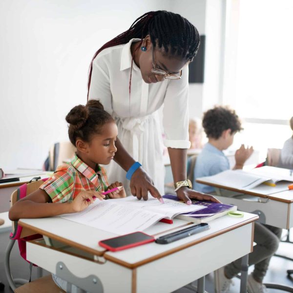 Teacher reading. Dark-skinned pleasant teacher standing near little girl and reading for her