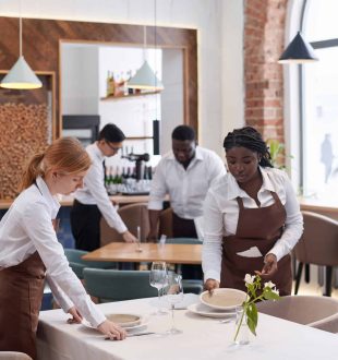 Vertical shot of ethnically diverse waiting team working in modern restaurant setting tables in morning